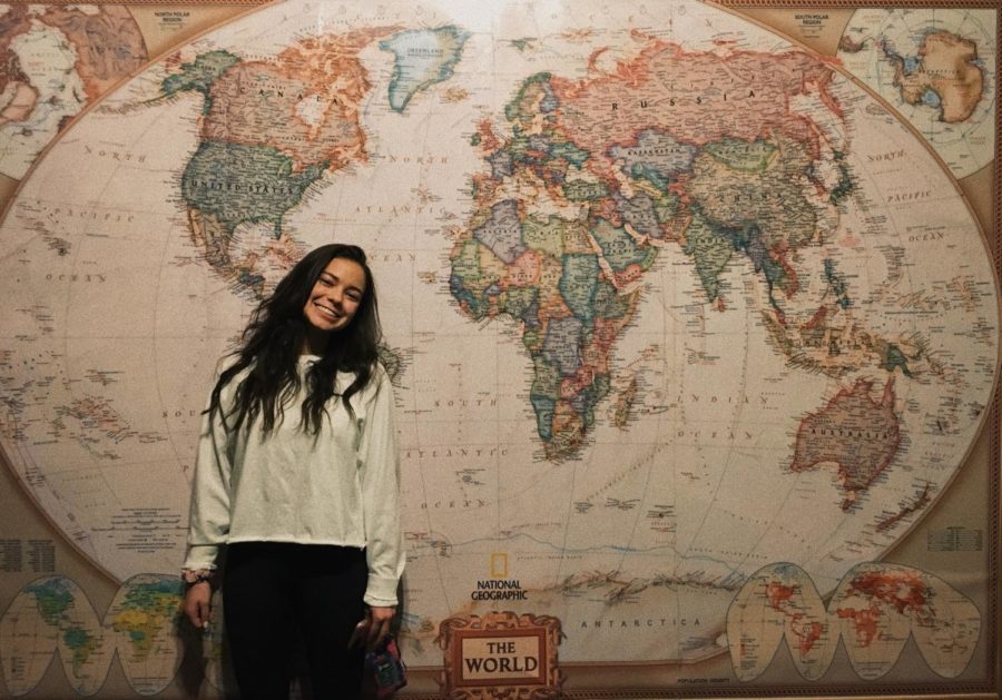 Junior Audrey Sandell posing with a smile in front of a world map at Kairos Coffee House.