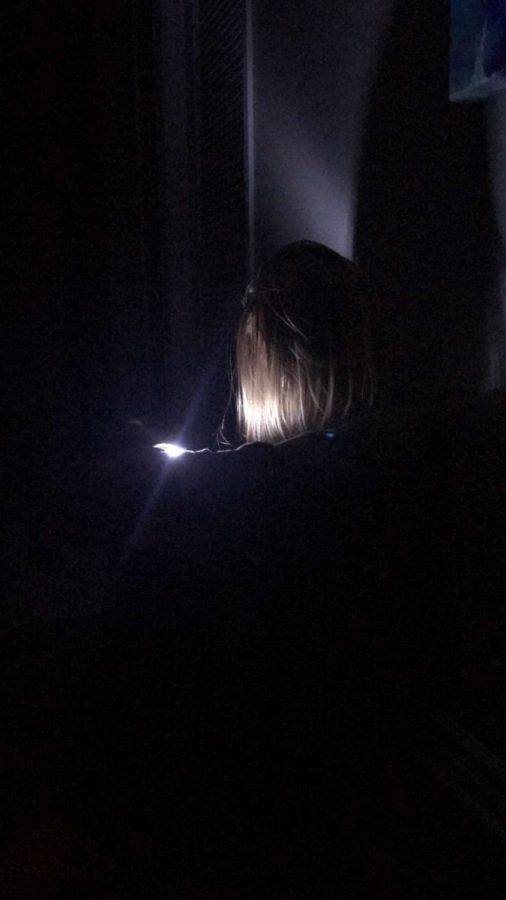 Sophomore Faith Poling, who has nyctophobia, sitting in the dark with only a small flashlight.