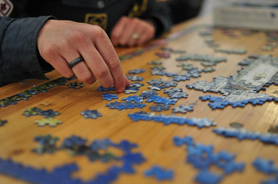 An individual attempts to solve this dark blue jigsaw puzzle. Labeled for Reuse by Creative Commons.