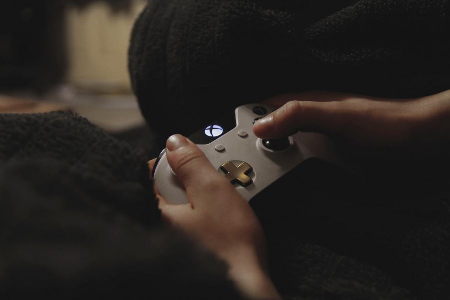 A person casually holding a white Xbox controller while playing a video game. Labeled for reuse by Unsplash.