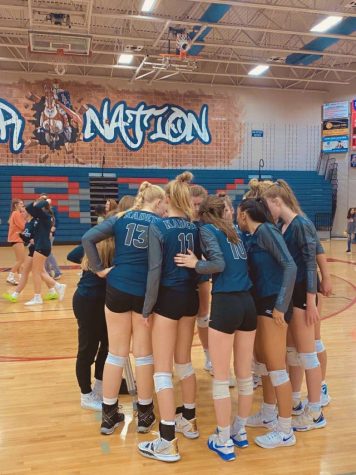 The varsity girls volleyball team gather in a huddle during an away game!