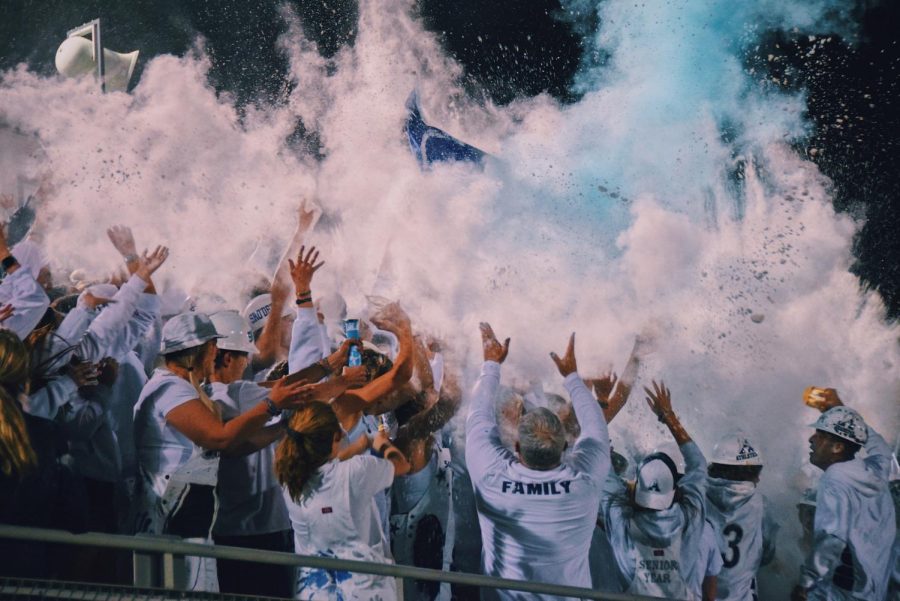 Students celebrate at a white-out-themed football game by throwing corn starch after scoring a touchdown. (Photo by Minta Williams).