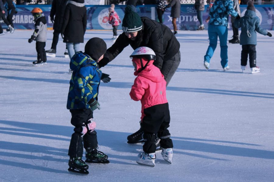 A young mom smiles as she helps her children ice skate around other families. Labeled free for reuse by Unsplash.