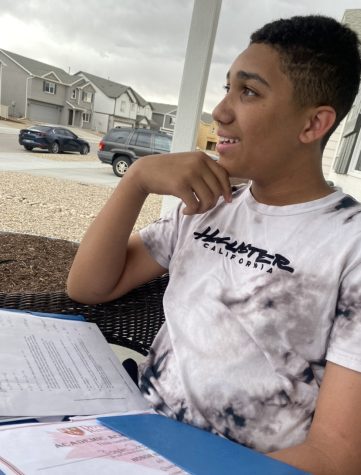 Shown is seventh grader Brayden Wilson sitting outside his house on the porch, smiling and doing his math homework.